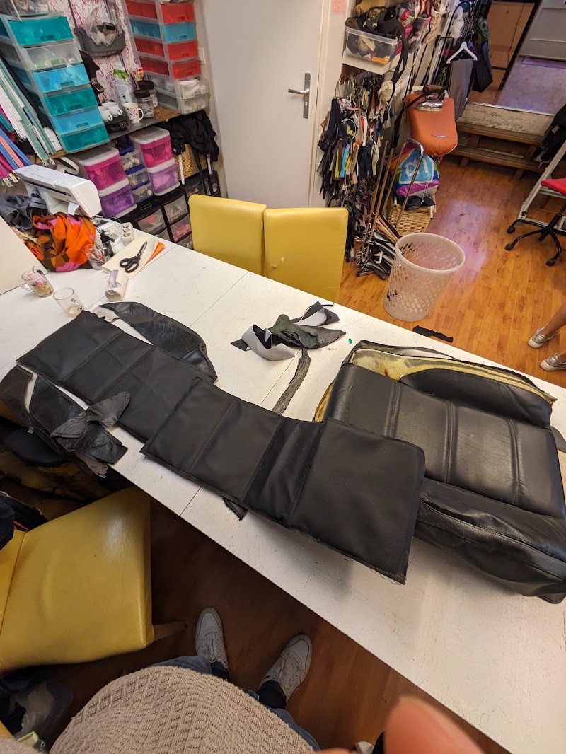Het atelier: de snijtafel met een leren autostoelbekleding erop, laden met garen en fournituren, en een rek met ritsen aan de muur.