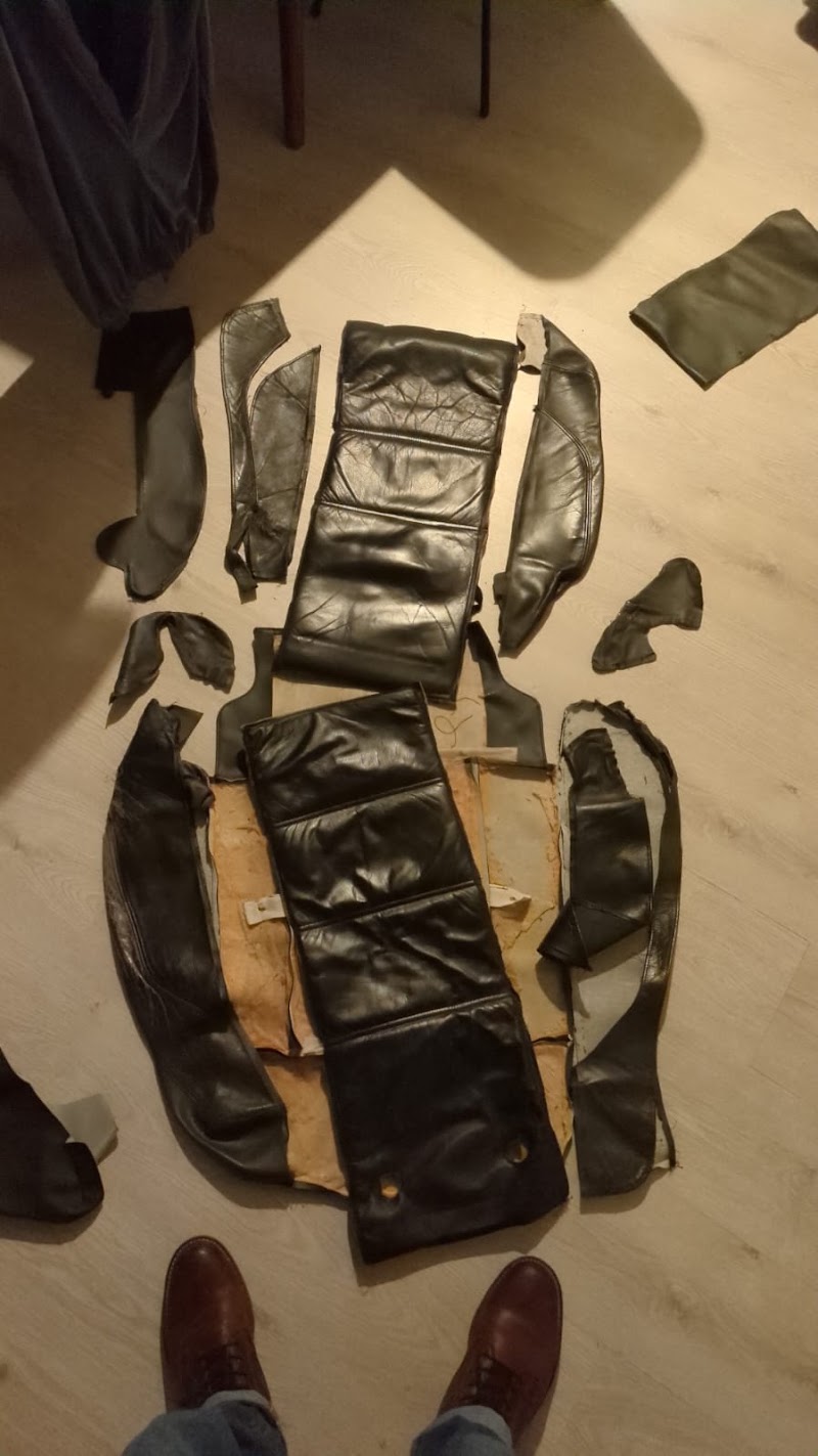 Een leren autostoelbekleding, volledig uit elkaar gehaald en per paneel uitgelegd op de werkvloer.